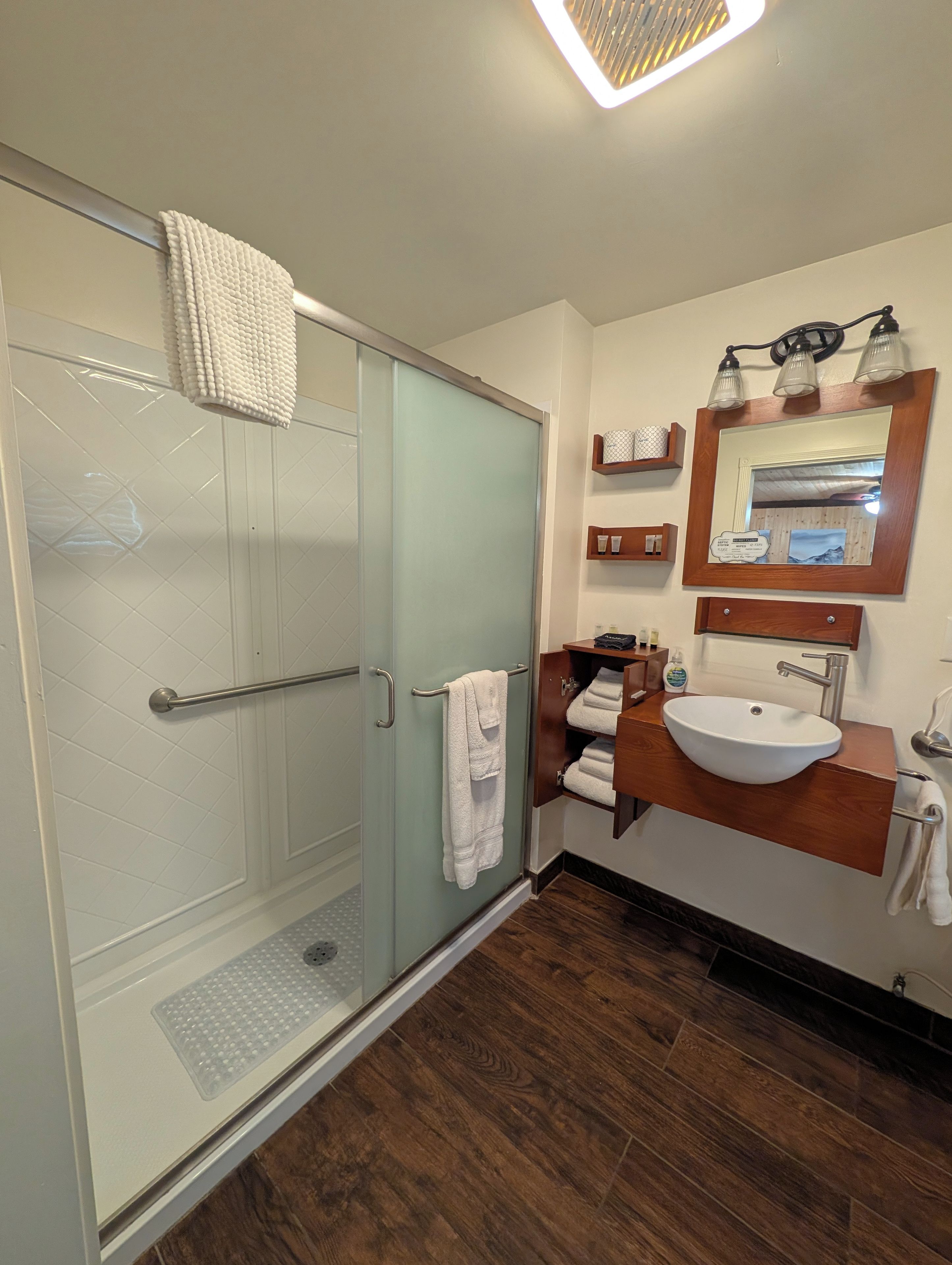 Un baño moderno con cabina de ducha de vidrio, tocador de madera con lavamanos y espejo con iluminación.