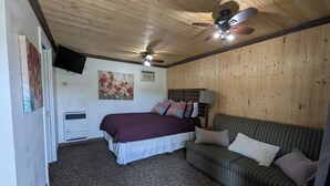 Ein Schlafzimmer mit einem Bett, einem grün gestreiften Sofa, einem Deckenventilator, einem angebrachten Fernseher und einem Bild an der Wand.