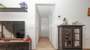 Een gang met een houten vloer, een televisie op een bureau, een kast met glazen deuren, en een klein model van een schip aan de muur.