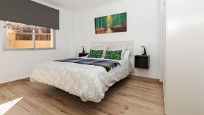 Een slaapkamer met een bed, een raam met verduistering, een schilderij aan de muur en een nachtkastje met een lamp.