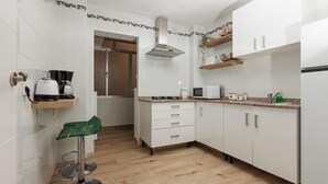 Een moderne keuken met witte kasten, een magnetron, een koffiezetapparaat en een kleine barkruk.