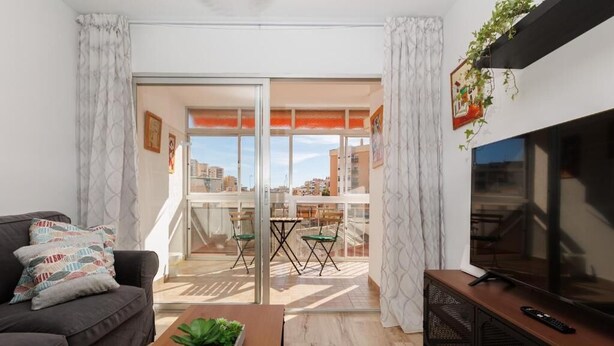 Een moderne woonkamer met een bank, salontafel, televisie en balkon met uitzicht op de stad.