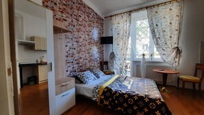 Et soveværelse med murstensvæg, seng med mønstret sengetøj, et garderobeskab, et lille bord og en stol.