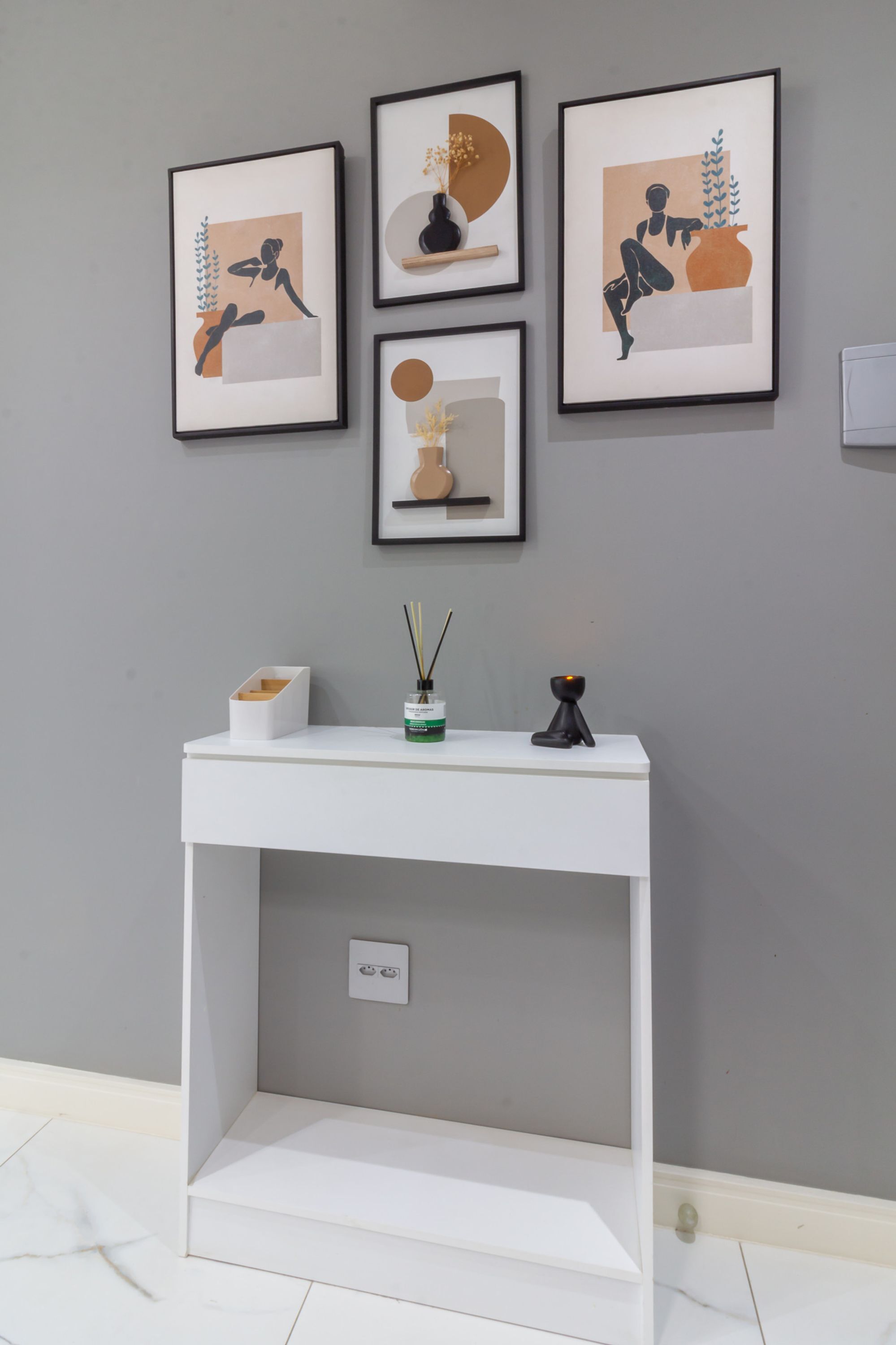 Una consola blanca con un florero y una vela, frente a una pared gris con cuatro obras de arte enmarcadas encima.