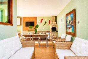A dining area with a brick oven, wicker furniture, and a painting on the wall. - Bz08 Casa 200m da praia de Geribá (Buzios)