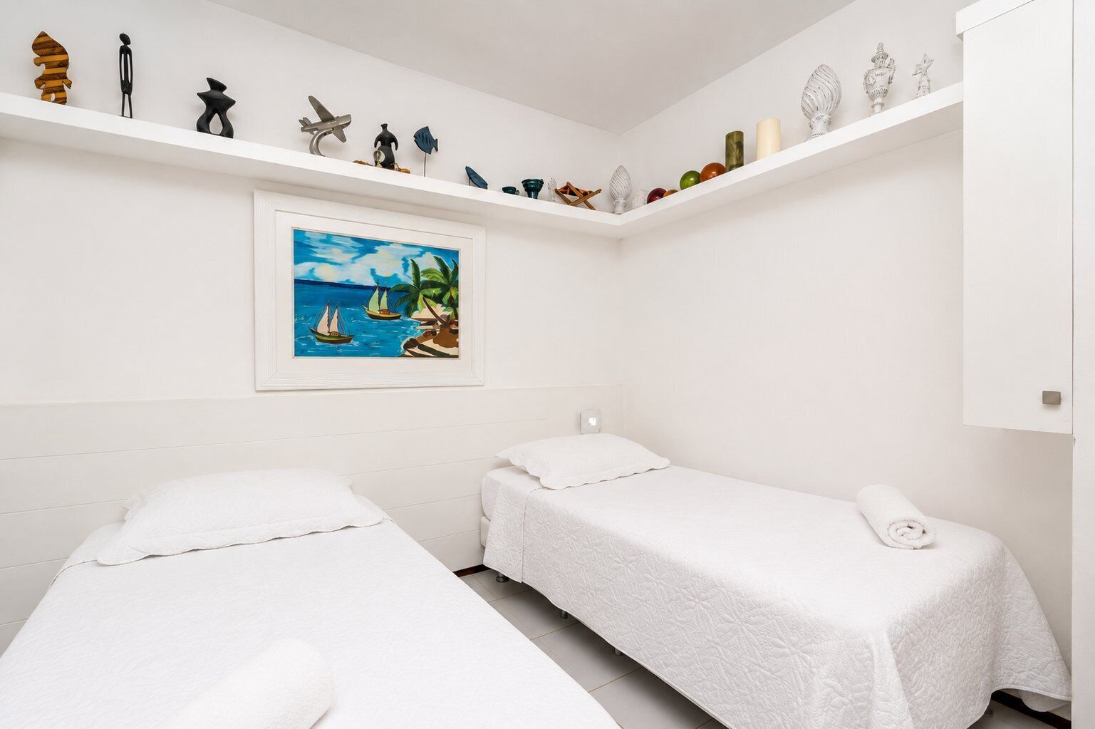 Une chambre d’hôtel avec deux lits, un tableau représentant un paysage tropical et divers objets décoratifs disposés sur les étagères.