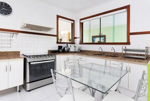 A modern kitchen with a gas stove, oven, and a glass dining table with chairs. - Bz08 Casa 200m da praia de Geribá (Buzios)