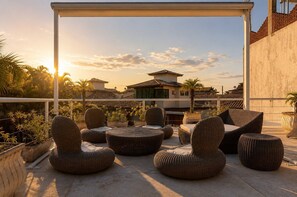 A rooftop terrace with wicker furniture, potted plants, and a view of traditional buildings. - Bz08 Casa 200m da praia de Geribá (Buzios)