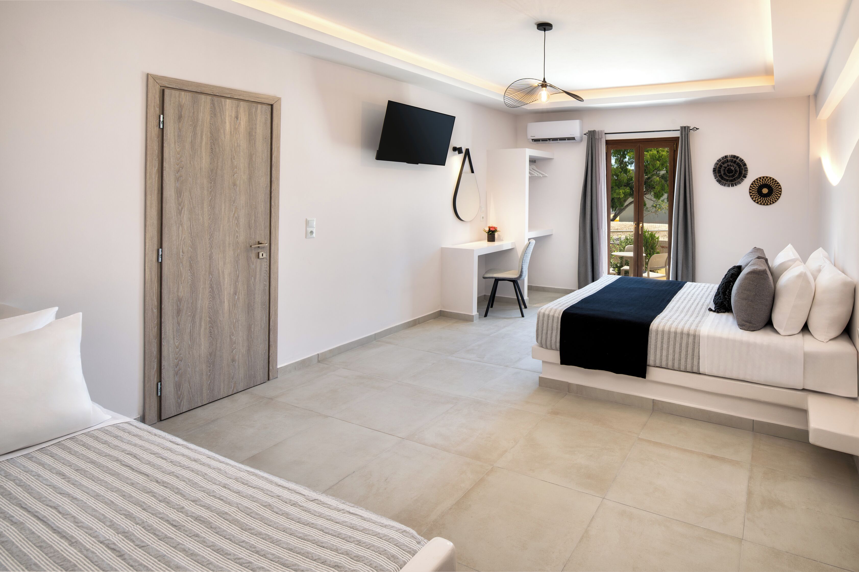 A modern hotel room with a bed, a desk, a TV, and a balcony with curtains.