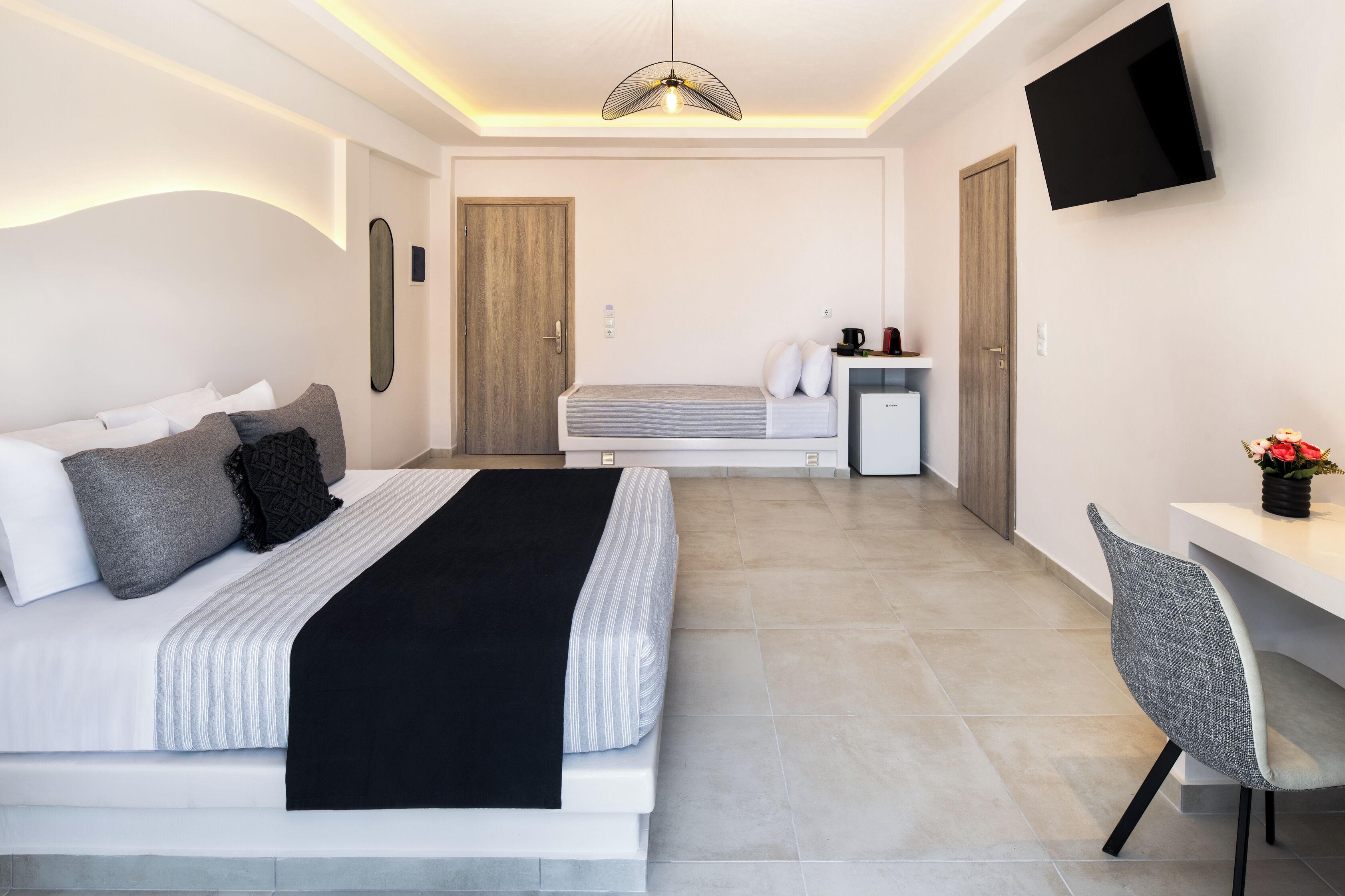 Ein modernes Hotelzimmer mit Bett, Nachttisch, Sessel, Schreibtisch, Fernseher und einer kleinen Küchenzeile.
