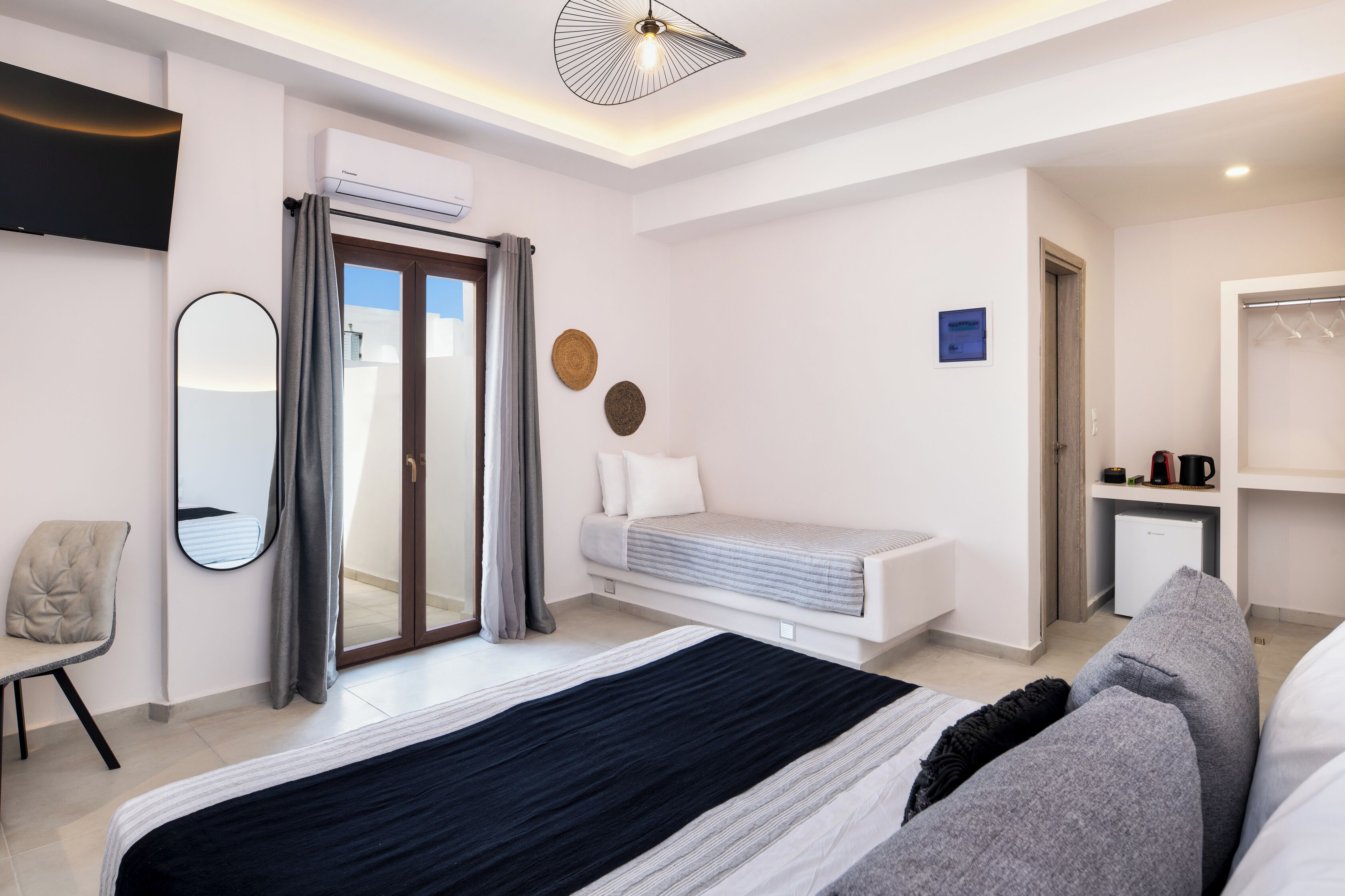 A modern hotel room with a bed, a chair, a desk, a television, and a wardrobe.