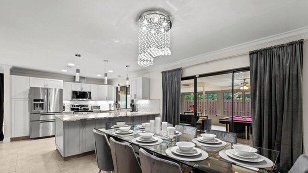 A modern kitchen with stainless steel appliances, a glass dining table set for four, and a view of the outdoor patio. - Modern, remodeled, pool table in Wellington! (Wellington)