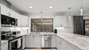 A modern kitchen with white cabinetry, granite countertops, stainless steel appliances, and recessed ceiling lights. - Modern, remodeled, pool table in Wellington! (Wellington)