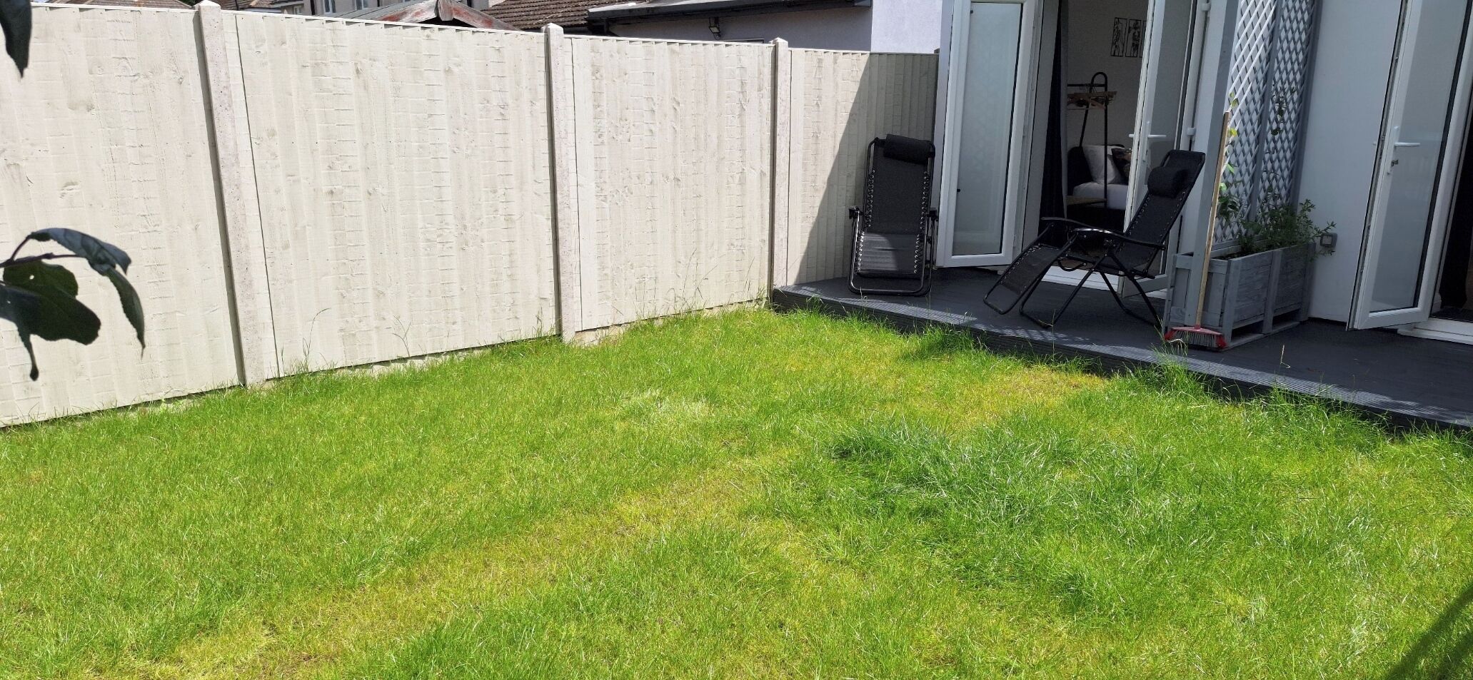 A backyard with a white fence, a lawn, and a patio area with outdoor furniture.