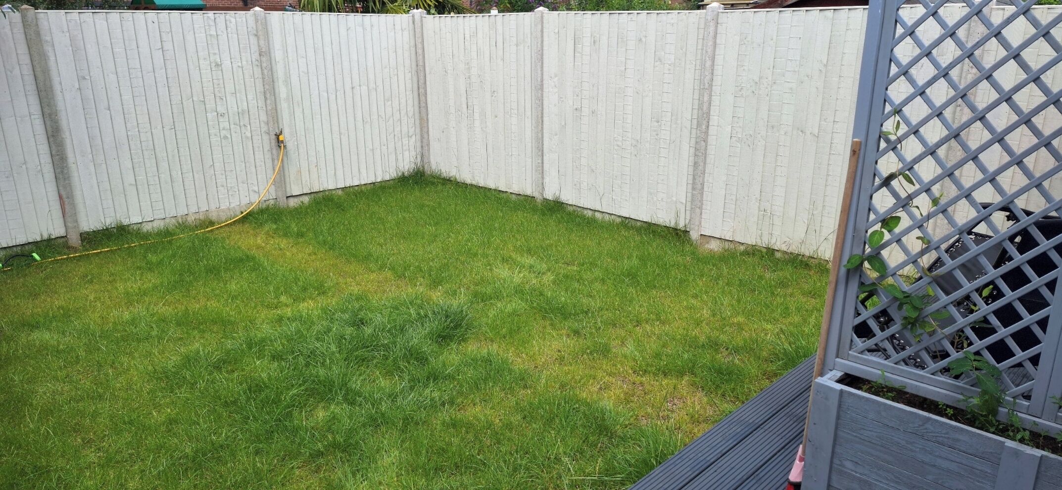 A fenced backyard with a grassy area and a wooden deck.