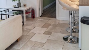 Una sala moderna con televisor de pantalla plana, sofá, mesa de centro, zona de bar con taburetes y un pasillo que lleva a otra habitación.