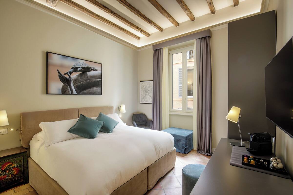 A modern hotel room with a large bed, a desk with a lamp, a television, and artwork on the walls.