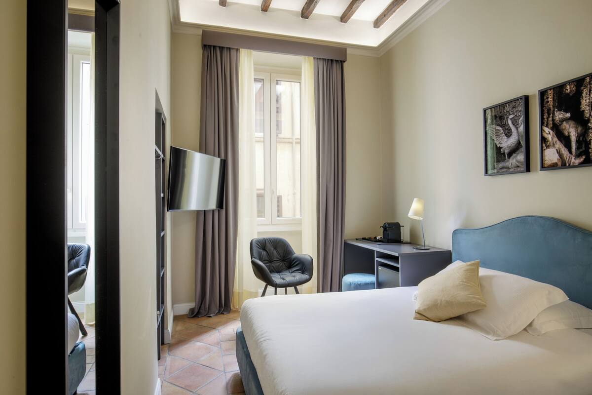 A hotel room with a bed, a desk, a chair, a TV, and two framed pictures on the wall.