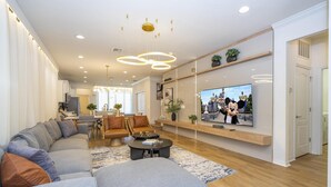 A modern living room with a large flat-screen TV, grey sofas, a coffee table, and a wooden floor. - 8941- Great Family Home near Disney, private pool - Windsor at Westside Resort (Kissimmee)