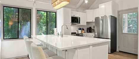 A modern kitchen with a large island, white cabinetry, and a hanging light fixture.