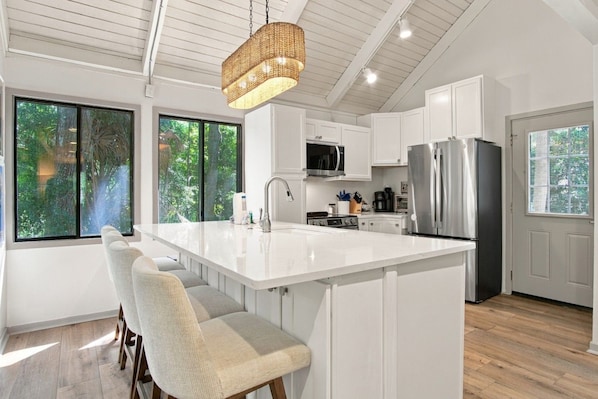 A modern kitchen with a large island, white cabinetry, and a hanging light fixture.