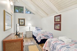 Ein Schlafzimmer mit zwei Betten, einem Schreibtisch, einer Lampe und gerahmten Bildern an den Wänden.