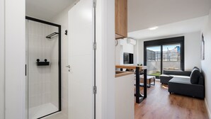 A modern apartment with a walk-in shower, a dining area with a wooden table and chairs, a sofa, and a large window with a view of a fence. - apartamento reformado con garaje de alquiler temporal (San Sebastián de los Reyes)