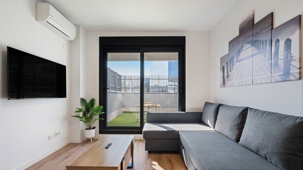 A modern living room with a grey sofa, a wooden coffee table, a mounted TV, and a potted plant. - apartamento reformado con garaje de alquiler temporal (San Sebastián de los Reyes)