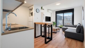 A modern kitchen with a sink, bar stools, and a wooden table. There is a sofa and a TV in the living area. - apartamento reformado con garaje de alquiler temporal (San Sebastián de los Reyes)