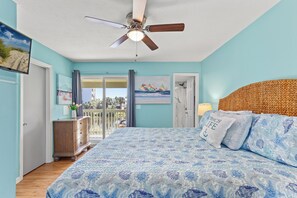 A bedroom with a bed, a ceiling fan, a dresser, a door, and a window with curtains. - Water-Front Home! The Best Amenities & 11 Pools! (Panama City Beach)