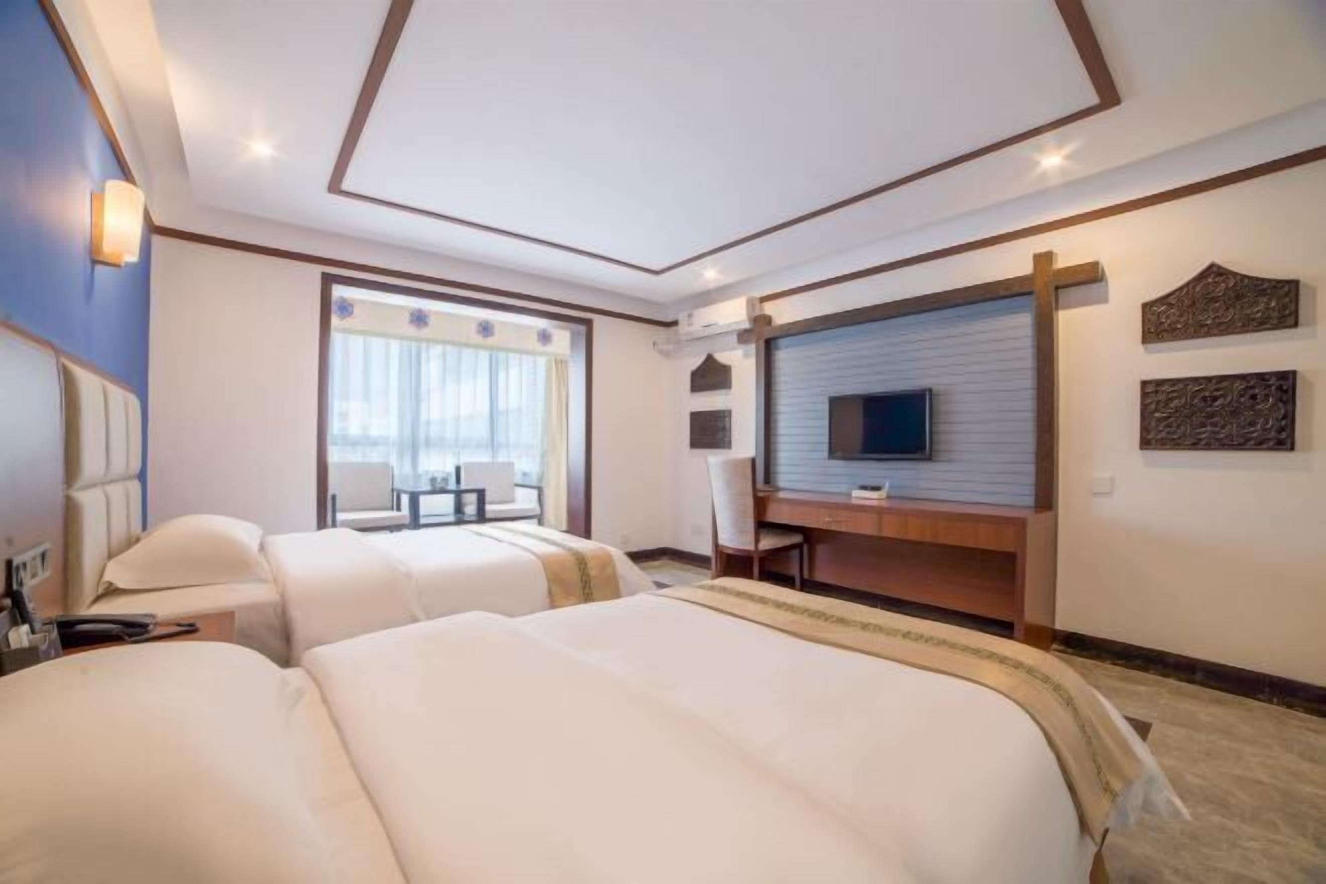 Habitación de hotel con dos camas, un escritorio, un televisor y una ventana con cortinas.