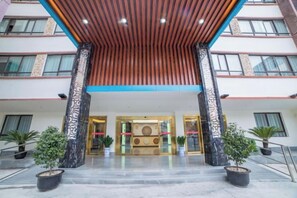 A hotel entrance with a wooden ceiling, a reception desk, and potted plants. - Xinguolv Hotel (Wenchuan)