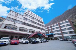 A multi-story building with a parking lot in front. - Xinguolv Hotel (Wenchuan)