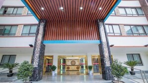 Entrada de hotel com design moderno, destacando teto de ripas de madeira, colunas de mármore e um balcão de recepção com painel decorativo.