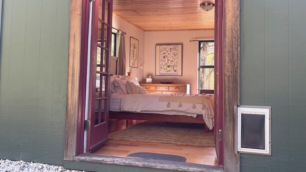 Un dormitorio con techo de madera, una cama con colcha blanca, una mesita de noche y una ventana.