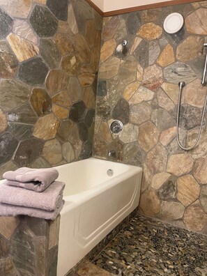 A bathroom with a stone wall, a bathtub, and a shower.
