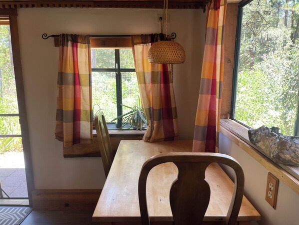 A wooden table and chair in a room with a window, curtains, and a hanging light fixture.