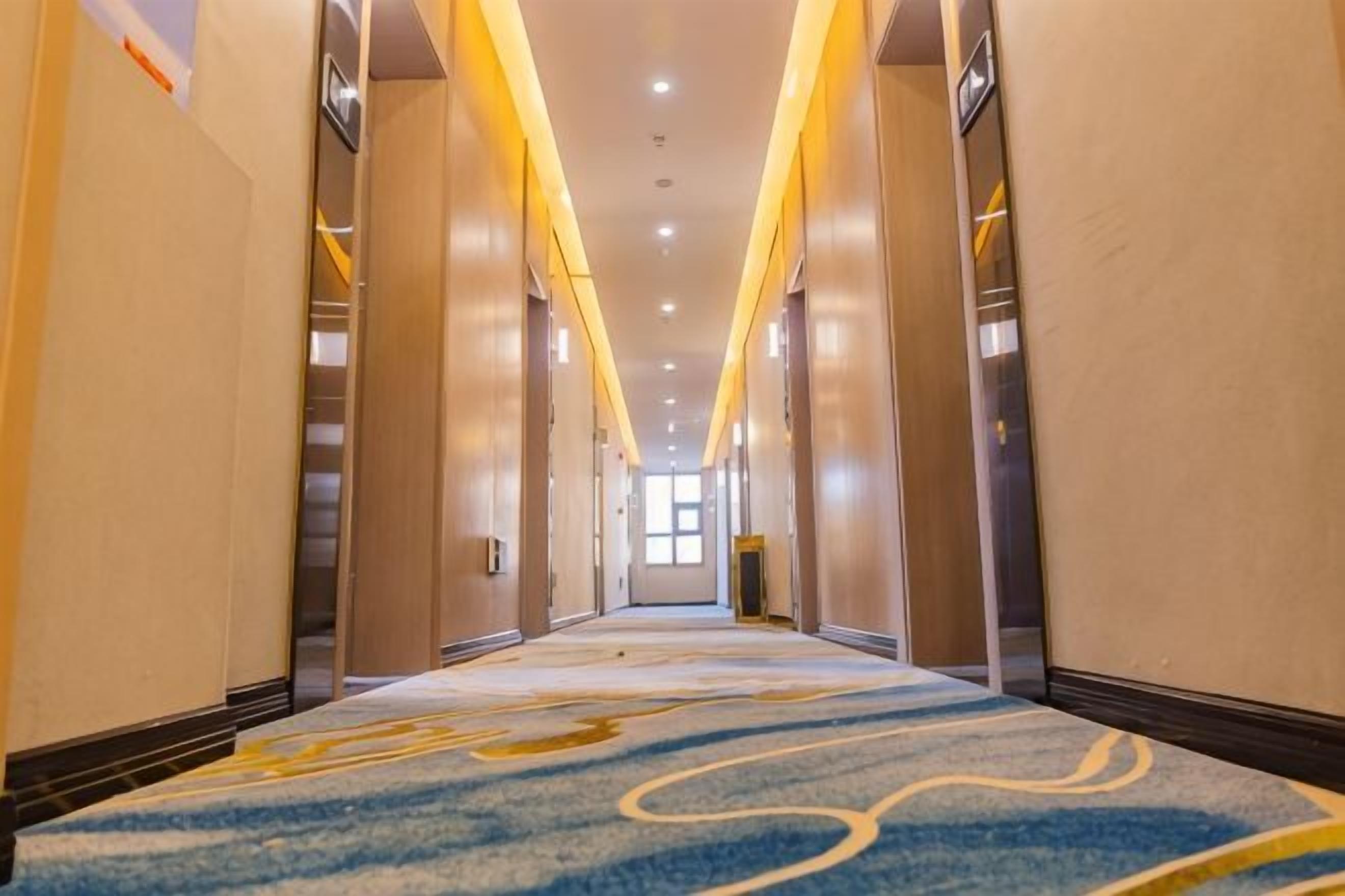 Un pasillo de hotel con piso alfombrado, puertas a ambos lados y un accesorio de iluminación en el techo.