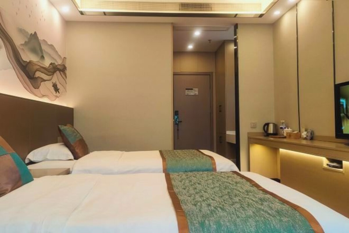 A hotel room with two beds, a wall-mounted TV, a small table with a kettle, and a door leading to another room.