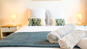 A neatly made bed with a blue bedspread and white pillows, two bedside lamps, and a floral artwork on the wall. - Harmonie en plein cœur du Vieil Annecy (Annecy)