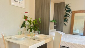 A modern, well-lit room with a white dining table set for two, a bed with a white mattress, and a large mirror. - Rotonde rue sommeiller (Annecy)