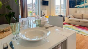 A dining area with a table set for two, a sofa, and a large window with a view of buildings. - Rotonde rue sommeiller (Annecy)