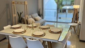 Un comedor moderno con una mesa de vidrio dispuesta para cuatro, sillas blancas y un espejo con marco de madera.