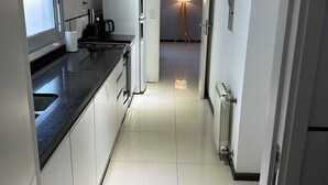 Una cocina moderna con armarios blancos, encimera negra y microondas integrado. Se observa una pequeña isla con un hervidor y una lámpara al fondo.
