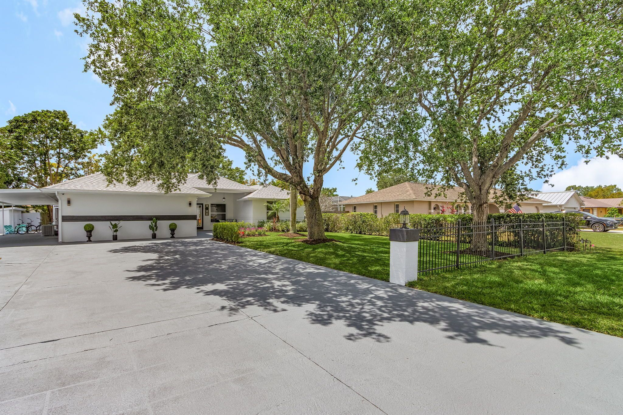 A residential area with a paved driveway, a large tree, and houses with white exteriors and dark trim.