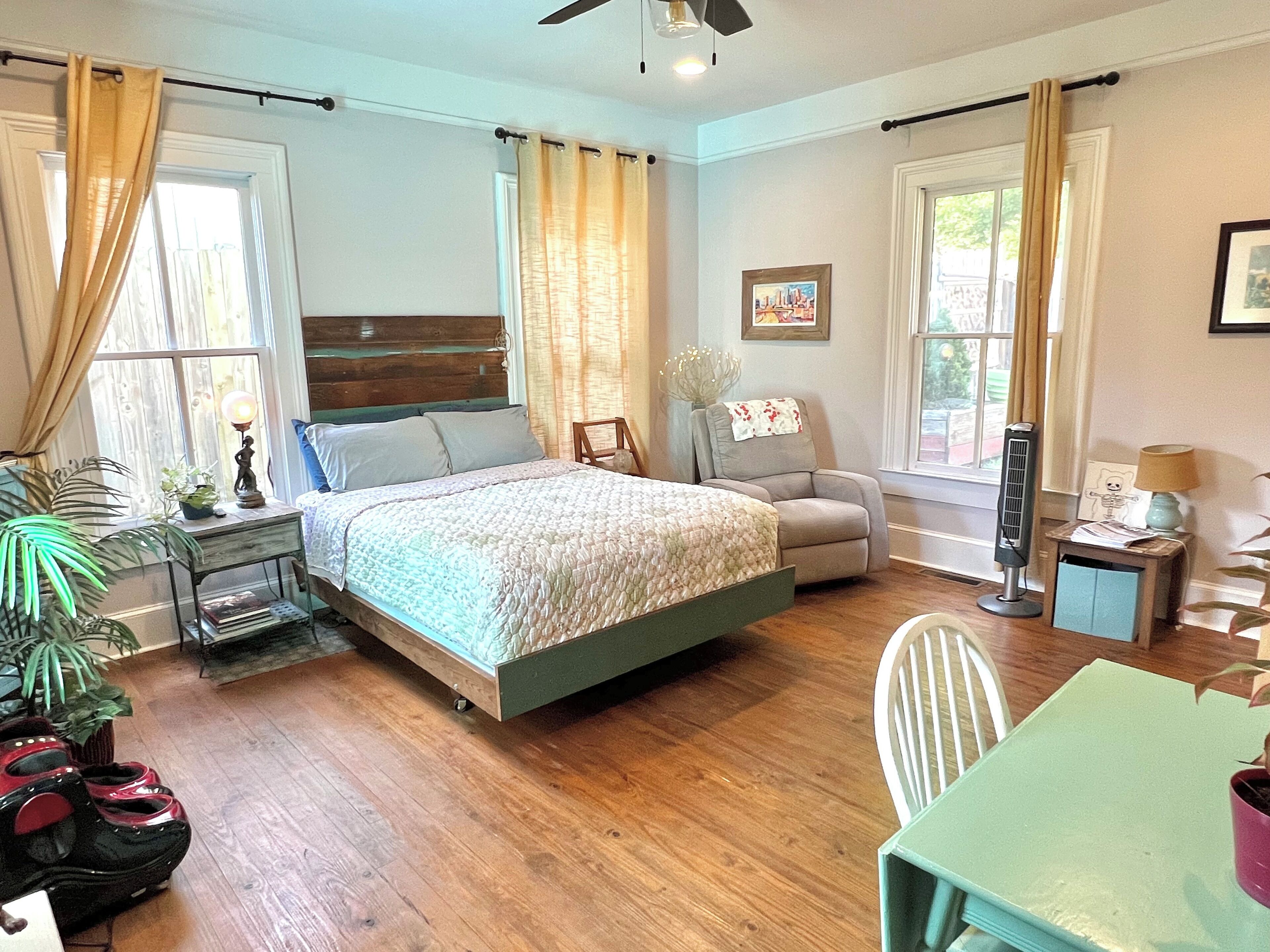 Quarto com cama, cadeira, mesa e ventilador.