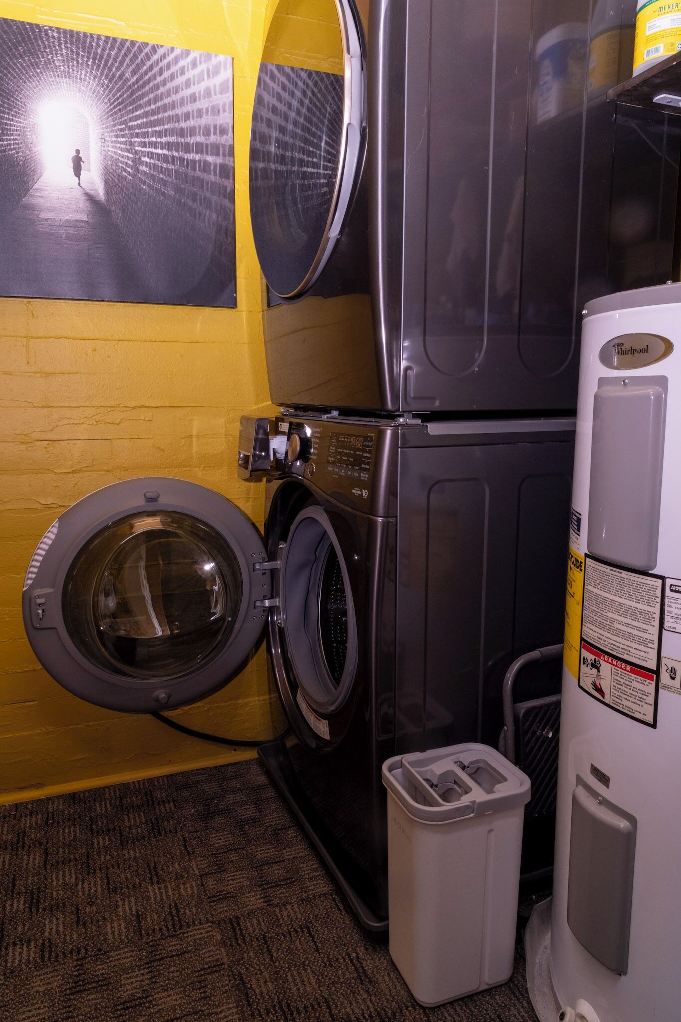 Een wasserette met een wasmachine, droger en een prullenbak.