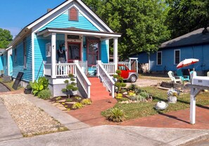 A blue house with a porch, a red car, and a mailbox.