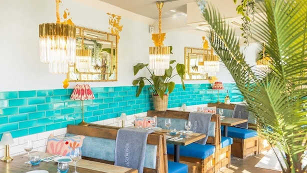 Un restaurante con cabinas de madera, paredes con azulejos verde mar y candelabros dorados colgantes.