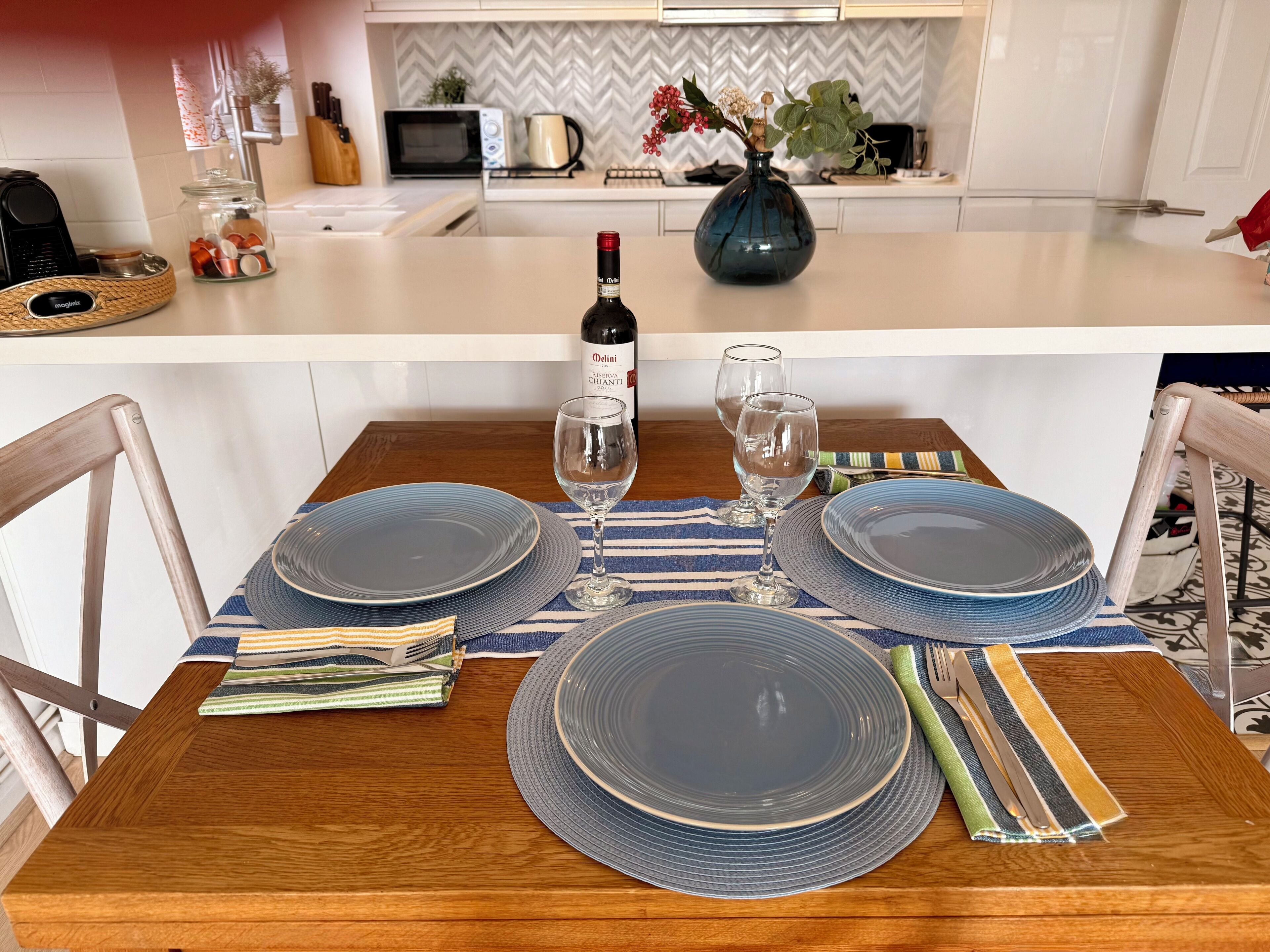 Een eettafel gedekt met blauwe borden, wijnglazen en een fles wijn.
